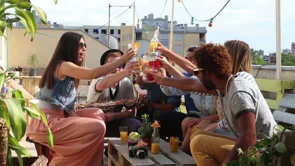 Cheerful multi-ethnic friends laughing and toasting with cocktails at rooftop