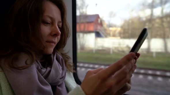 Woman Passenger of Suburban Train Is Using Smartphone, Sitting Near Window, Portrait