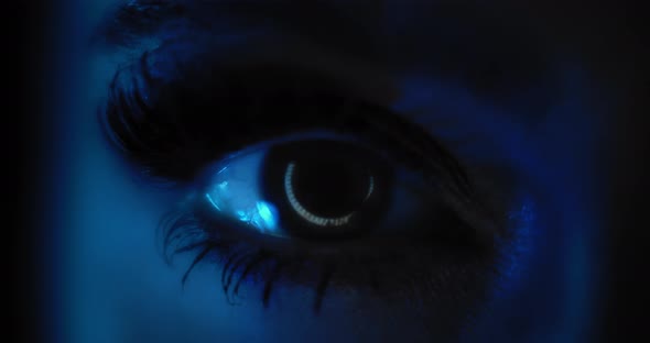 Close up of a woman's eye with beautiful make up opening in a dark blue lighting