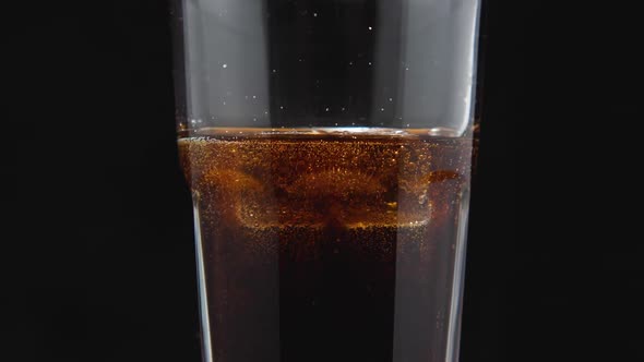 A close-up of a glass with ice cubes and a dark carbonated drink on the kitchen board