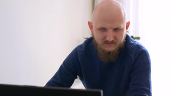 A Bald Man with a Beard and Blue Eyes Works Intently at the Computer