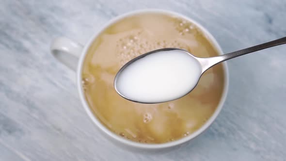 A spoonful of milk in close-up over a white cup of fresh hot tea on a wooden table