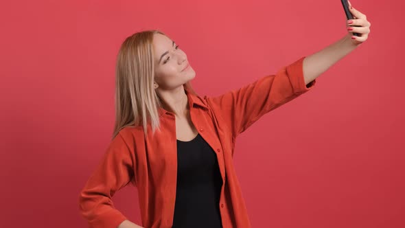 Funny Young Blonde Haired Woman Taking Selfie on Red Background