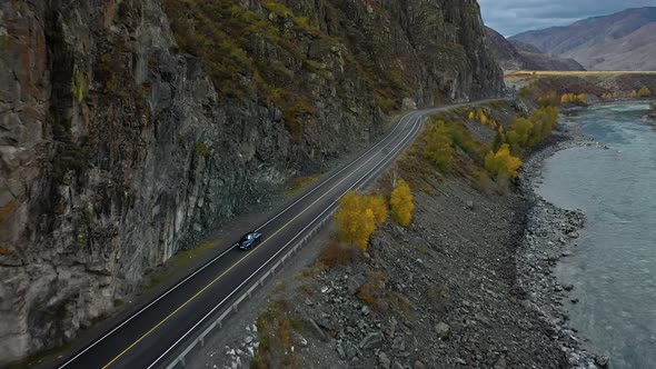 Blue Car Drives Along the Road in the Mountains Along the River