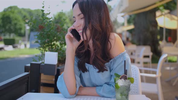 Pretty Brunette Woman Sitting in Outdoor Restaurant and Talking Her Mobile Phone