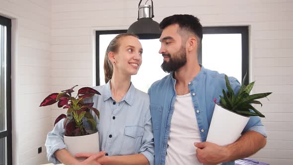 Young Family Standing in a New House with Flowers in Their Hands and Posing for the Camera