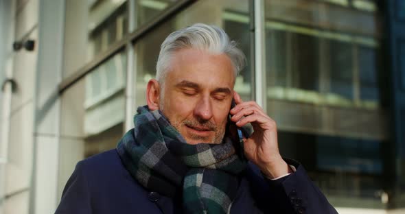 A Grayhaired Warmly Dressed Man Talking on a Mobile Phone While Walking in City