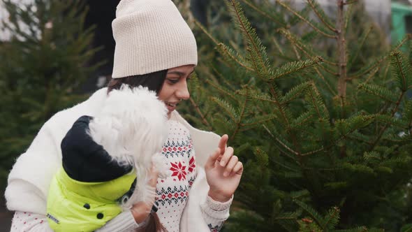 Woman with a White Dog in Her Arms Near a Green Christmas Trees