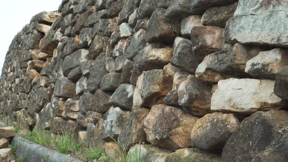 Destroyed retaining wall made of natural brown stone along the road with a border 