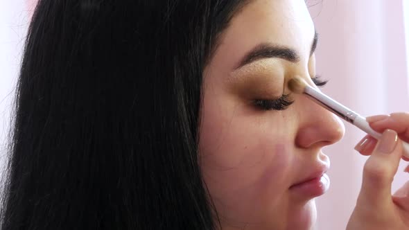 Girl Stylist Makes a Stylish Bright Makeup to a Young Beautiful Woman Model in the Studio