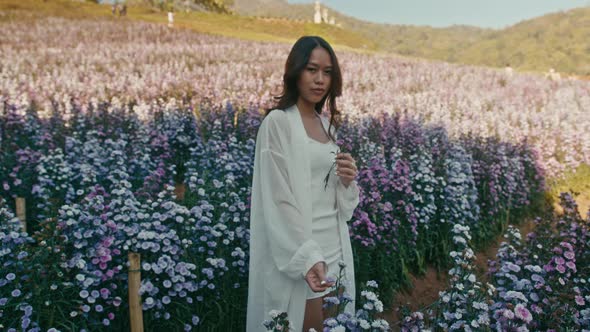 Young Asian Woman in Flower Field on Sunset Look at Camera