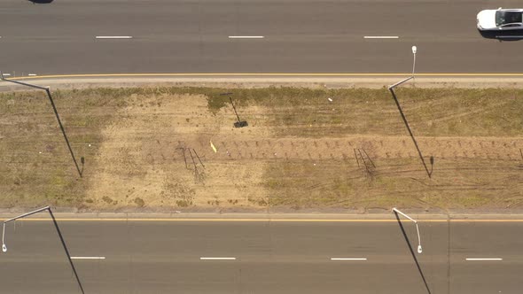A top down view directly over a highway median on a sunny day. With light traffic on either side of
