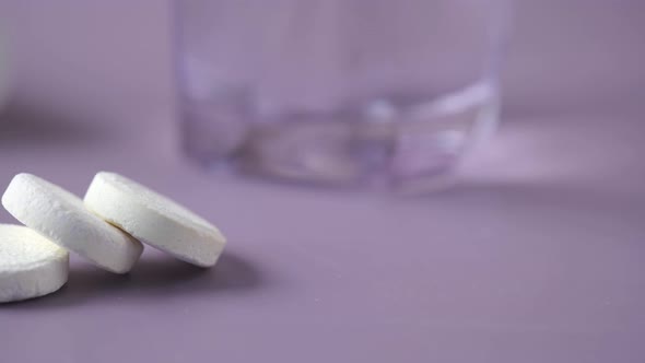 Effervescent Soluble Tablet Pills and Glass of Water on Purple Background