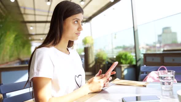 Pretty Woman Using Smart Phone Sitting in a Cafe Writing Message