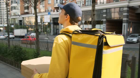 Back View of Delivery Man with Yellow Thermo Backpack Delivering Pizza Order While Walking on Urban