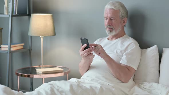 Success Old Man Celebrating on Smartphone in Bed