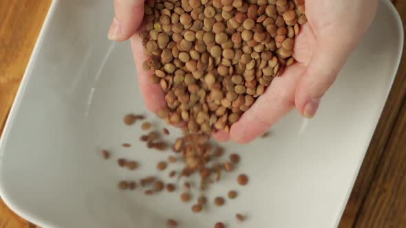 Closeup of a Woman's Hands Pouring Dry Raw Green Lentils Into a Plate