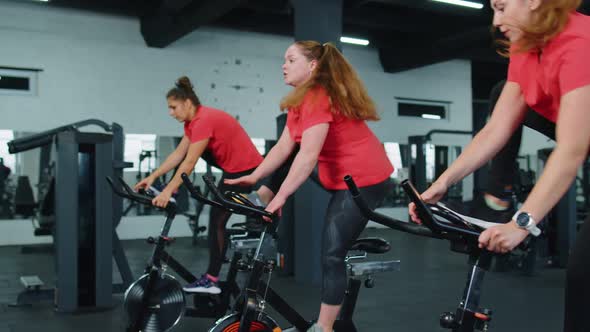 Healthy Caucasian Group of Women Exercising Workout on Stationary Cycling Machine Bike in Gym