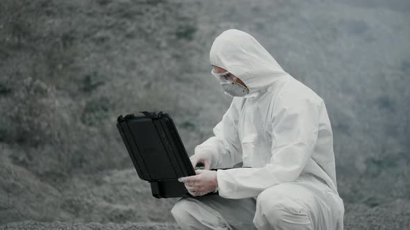 A lab technician in a mask and chemical protection suit opens a toolbox