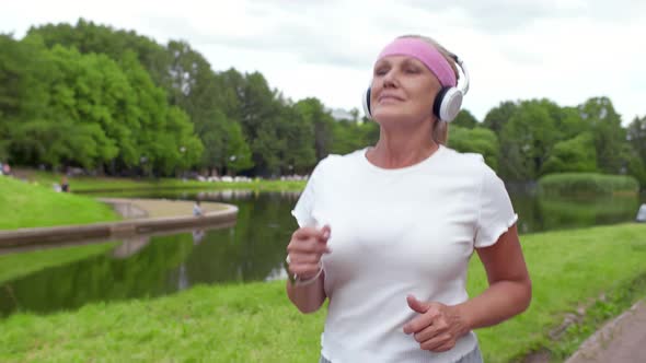Mature Woman in Headphones Jogging in Summer Park