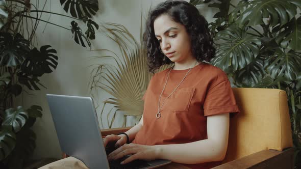 Mixed Race Girl in Armchair and Using Laptop in Room with Plants