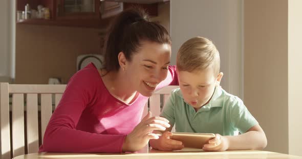 Mother And Child Playing On A Mobile Phone At The Table Having A Good Time Together