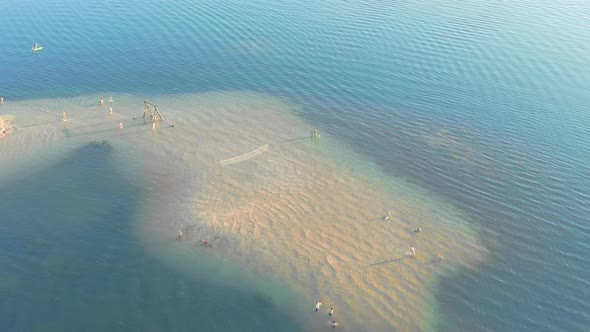 Atoll with Tropical Beach Island Surrounded By Water with a Volleyball Court and Resting People