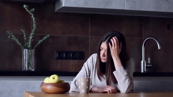 Woman With Headache Sitting In Kitchen