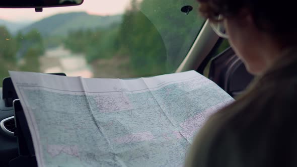 Traveler Girl Sits In The Car Looks At The Map. A Young Active Girl Engaged In Hiking Came Place