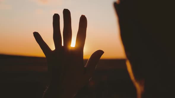 Girl Looks at the Sun Through Her Hand at Sunset