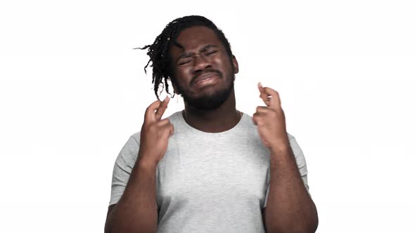 Portrait of Praying African American Man in Casual Tshirt with Afro Pigtails Keeping Fingers Crossed