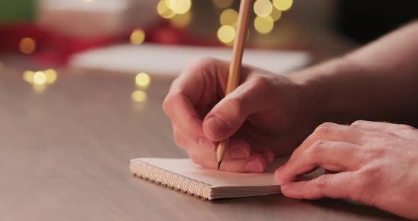 Man Writes Shopping List Holidays Notepad Pencil Under Warm Light Evening