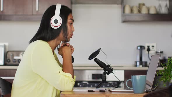 Mixed race gender fluid person recording a podcast using laptop reading notes at home