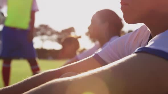 Female soccer player sitting on the ground next to teammates on soccer field. 4k