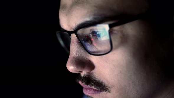 Closeup face of young man with glasses which reflects computer screen, front view. Man with glasses