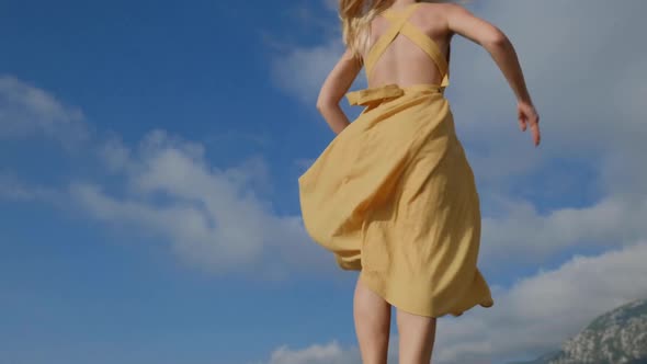 Dancing blonde woman in a yellow dress  against the background of mountains in Montenegro.