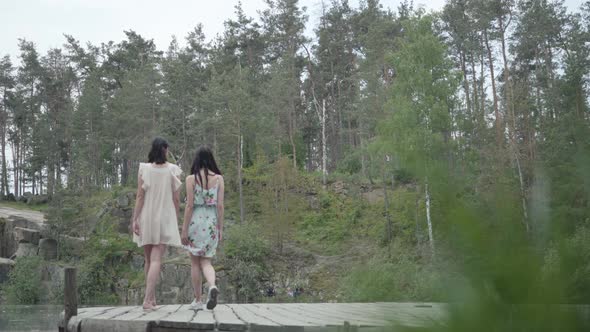 Two Cute Young Women Wear Summer Dresses Standing in the Top of Rock and Looking at Nature