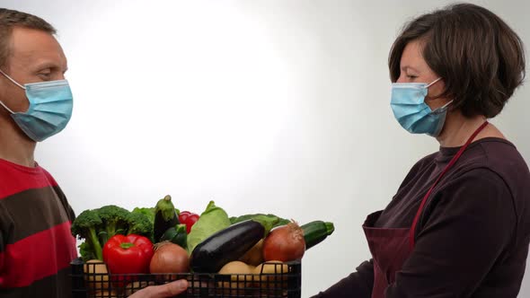 A Volunteer Distributor Handing a Box to a Masked Woman with Fresh Vegetables for Those in Need