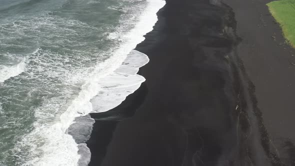 Black sand beach with waves in Vik, Iceland with drone video above moving back.