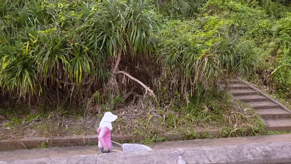 Woman with face covereding a wheelbarrow full of gravel on the island of Cat Ba Vietnam, Side view t