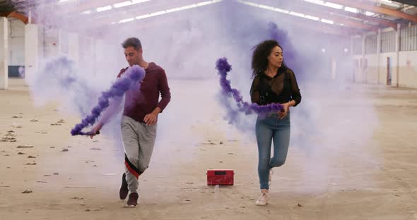 Dancers in an empty warehouse holding smoke grenade