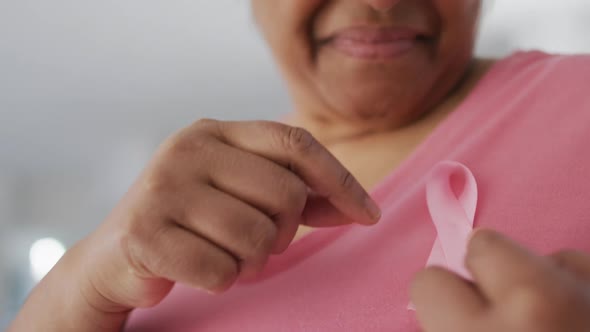 Midsection of smiling african american senior woman in pink t shirt and pink breast cancer ribbon