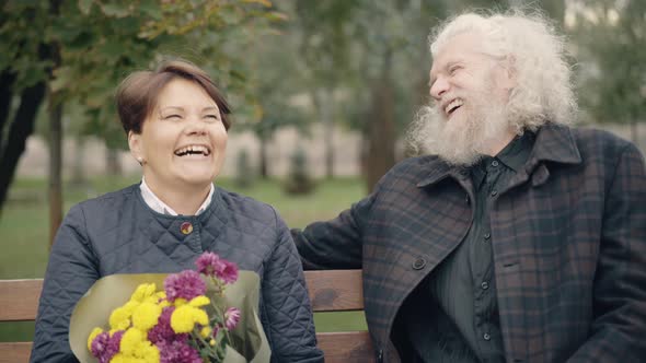Laughing Relaxed Senior Couple Sitting on Bench Enjoying Spring or Autumn Day Outdoors