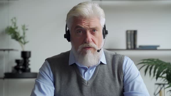 An Elderly Businessman in a Headset Having a Video Conference with a Business Partner Working in an