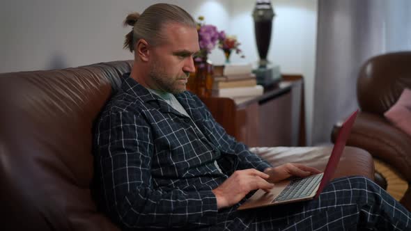 Side View Portrait of Busy Focused Caucasian Man Surfing Internet on Laptop Sitting in Home Office