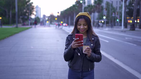 Carefree Young African American Woman in Stylish Leather Jacket Messaging with Smartphone in the