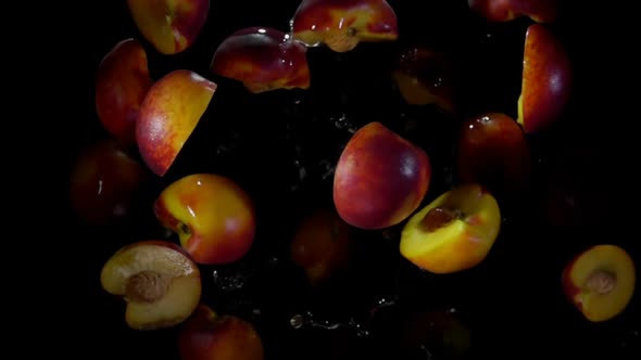 Halves of a Wet Peach are Bouncing with Drops of Water on a Black Background
