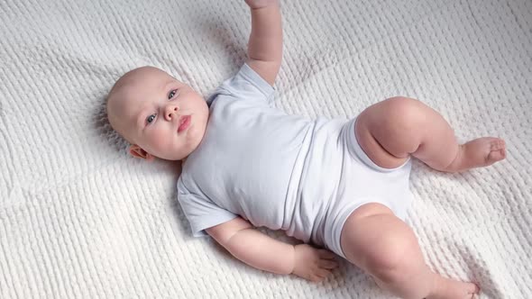 Happy Naked Baby in Diaper Lying on His Back on the White Sheet