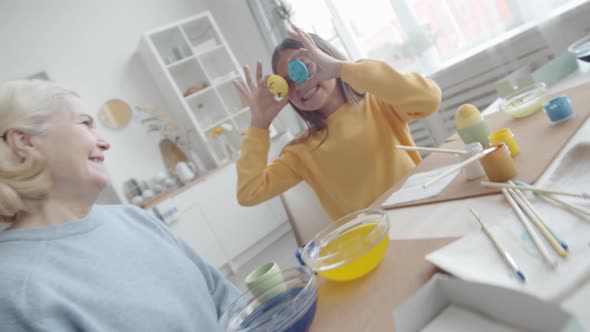 Joyous Girl Holding Easter Eggs in front of Eyes and Posing for Camera