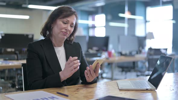 Angry Middle Aged Businesswoman Feeling Annoyed While Using Smart Phone in Office